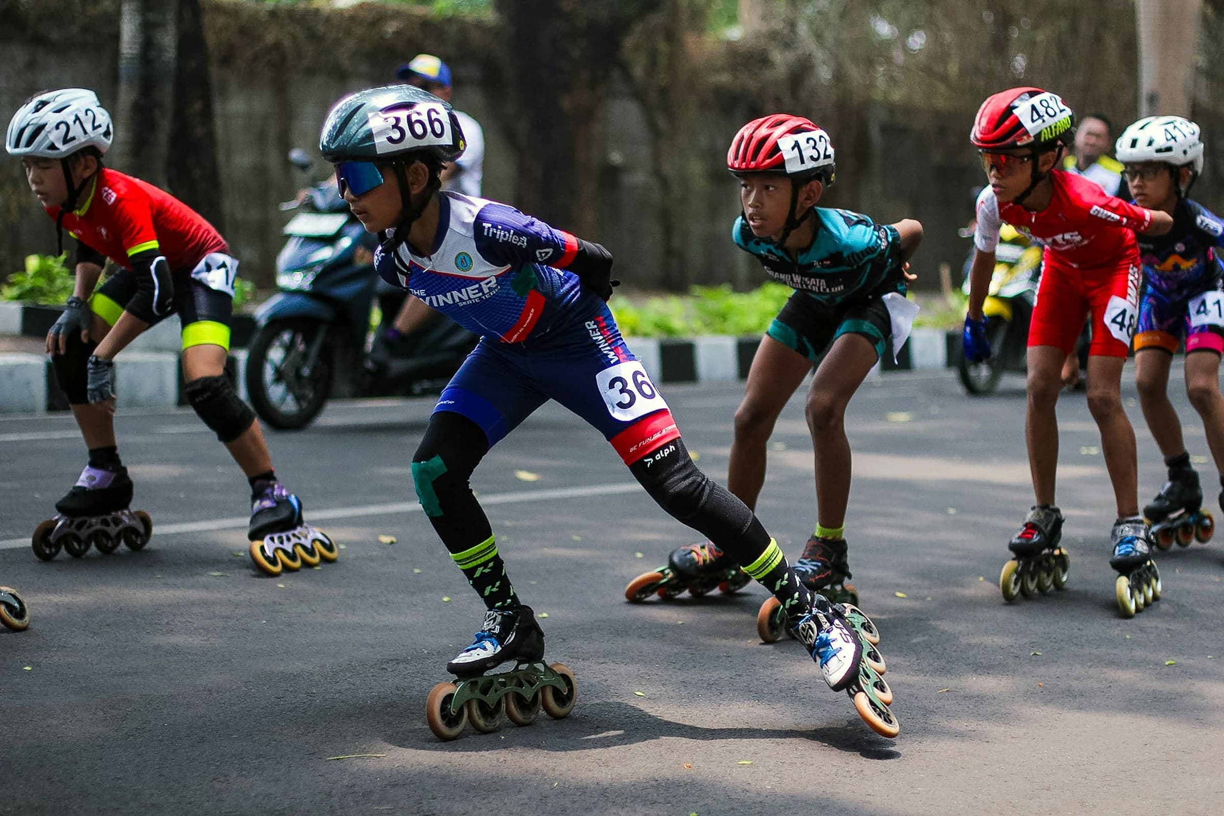 Junior inline speed skaters in race bibs and helmets skating in a tight, disciplined pack