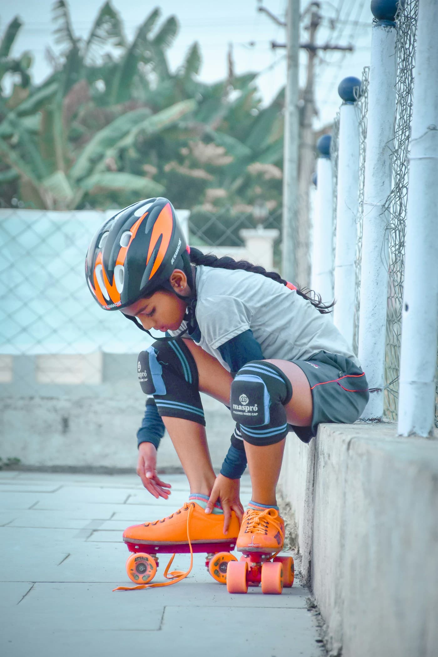 Young skater in helmet and knee pads lacing up a pair of orange quad skates