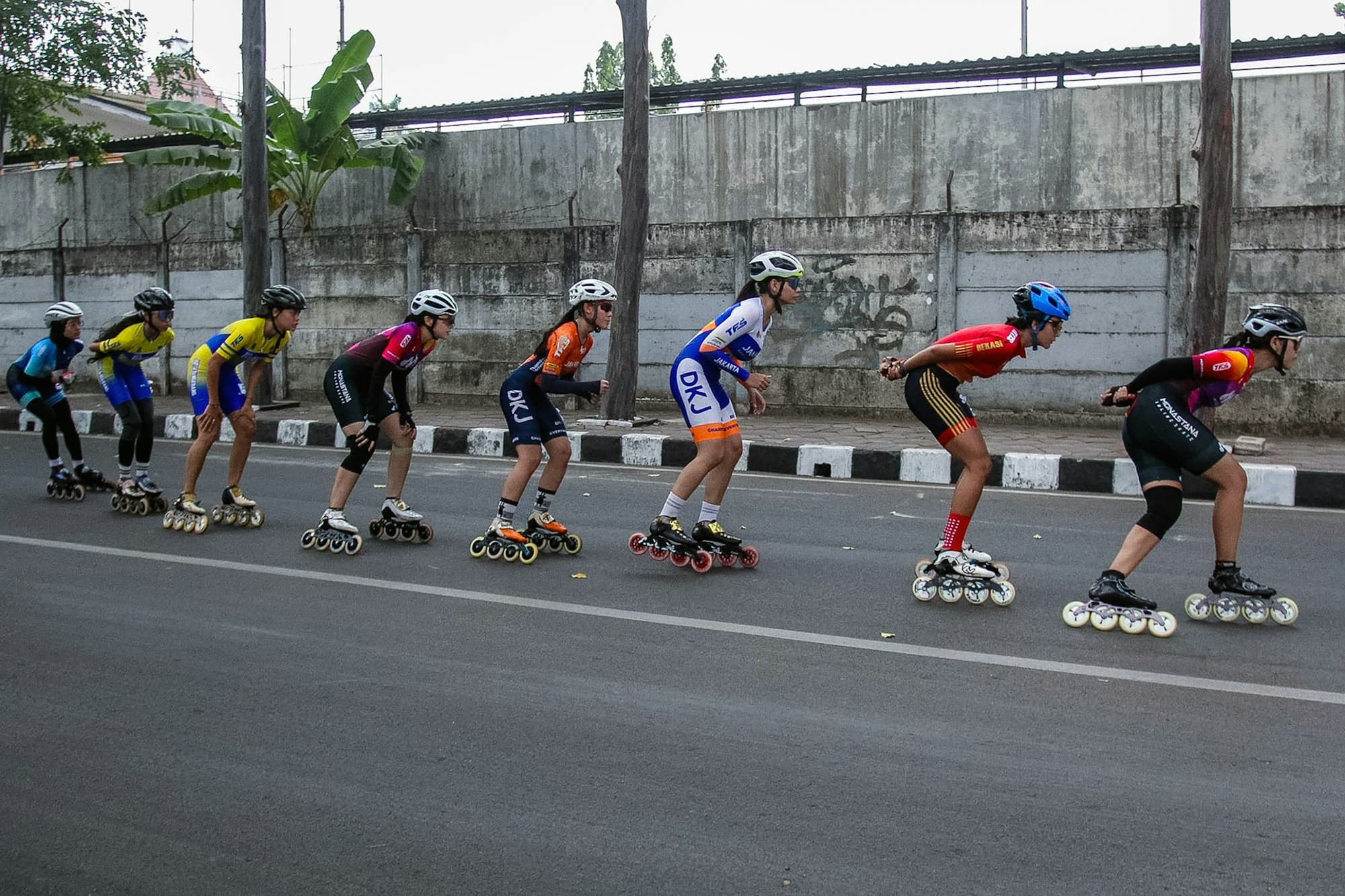 A pack of young inline speed skaters racing in a low tuck along a road